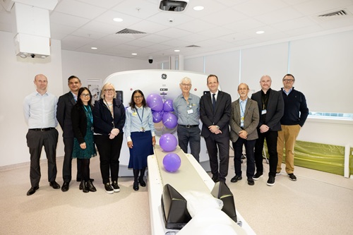 Group of people standing in front of a PET scanner decorated with purple balloons.